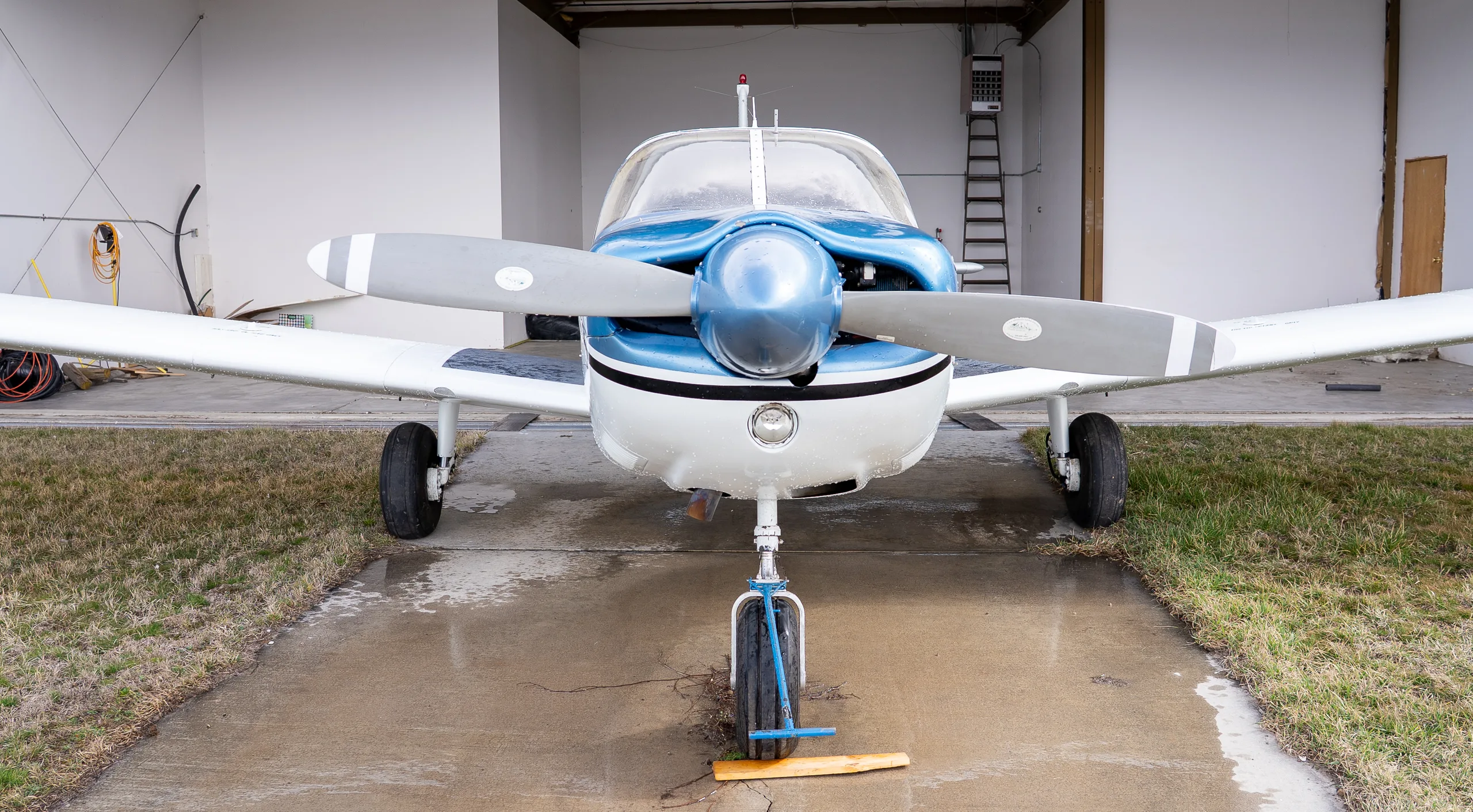 Front view of a white and blue single-engine propeller aircraft parked in a hangar.
