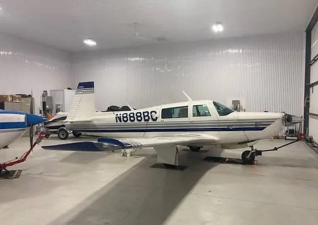 A white single-engine aircraft with blue and grey stripes, registration N888BC, parked inside a hangar.