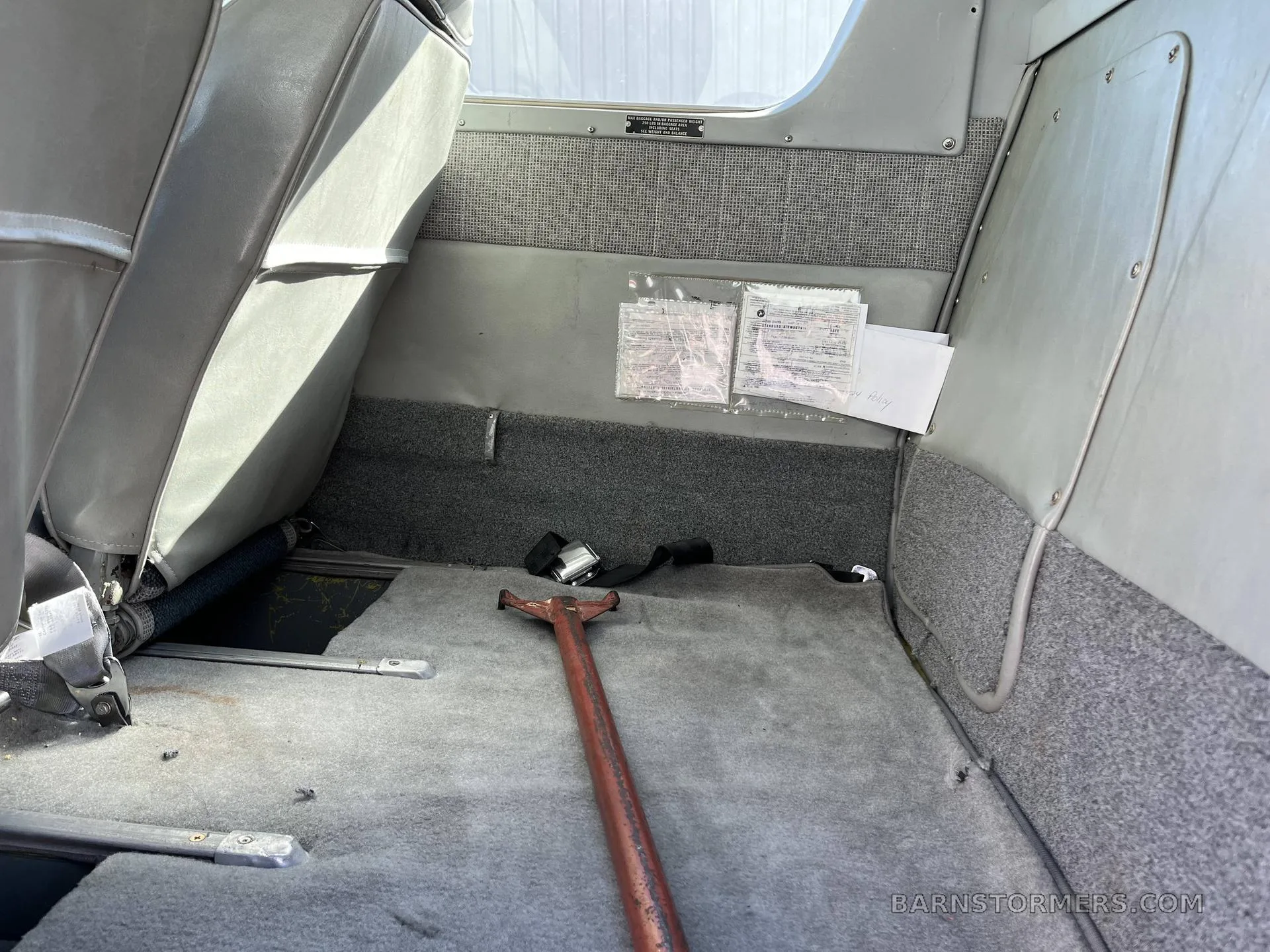 The rear cabin area of the aircraft shows grey carpet, the back of a seat, and a red tow bar on the floor.