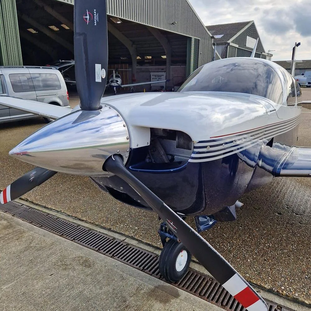 A close-up view of the polished chrome spinner and propeller of a white and blue single-engine aircraft, N91727, parked on an airfield.