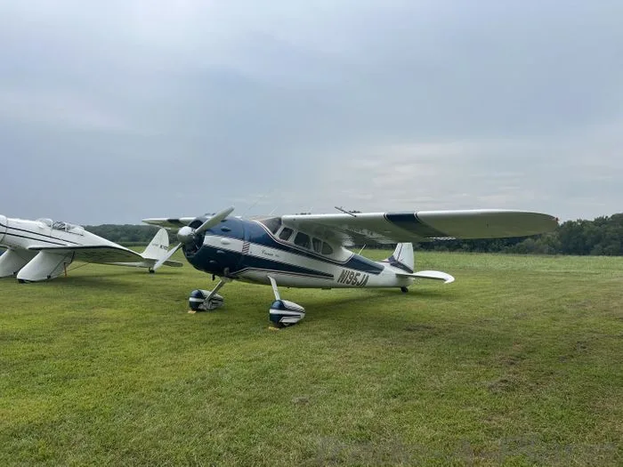 A blue and white Cessna 195 aircraft with tail number N195JA parked on a grassy field.