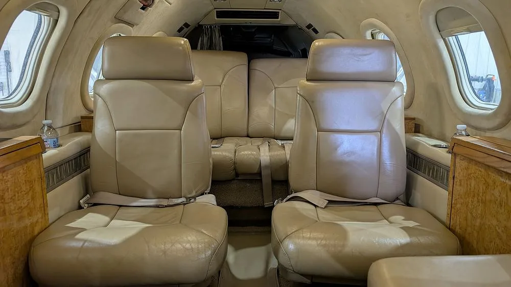 The aircraft's cabin interior features two forward-facing beige leather seats and a rear bench seat.