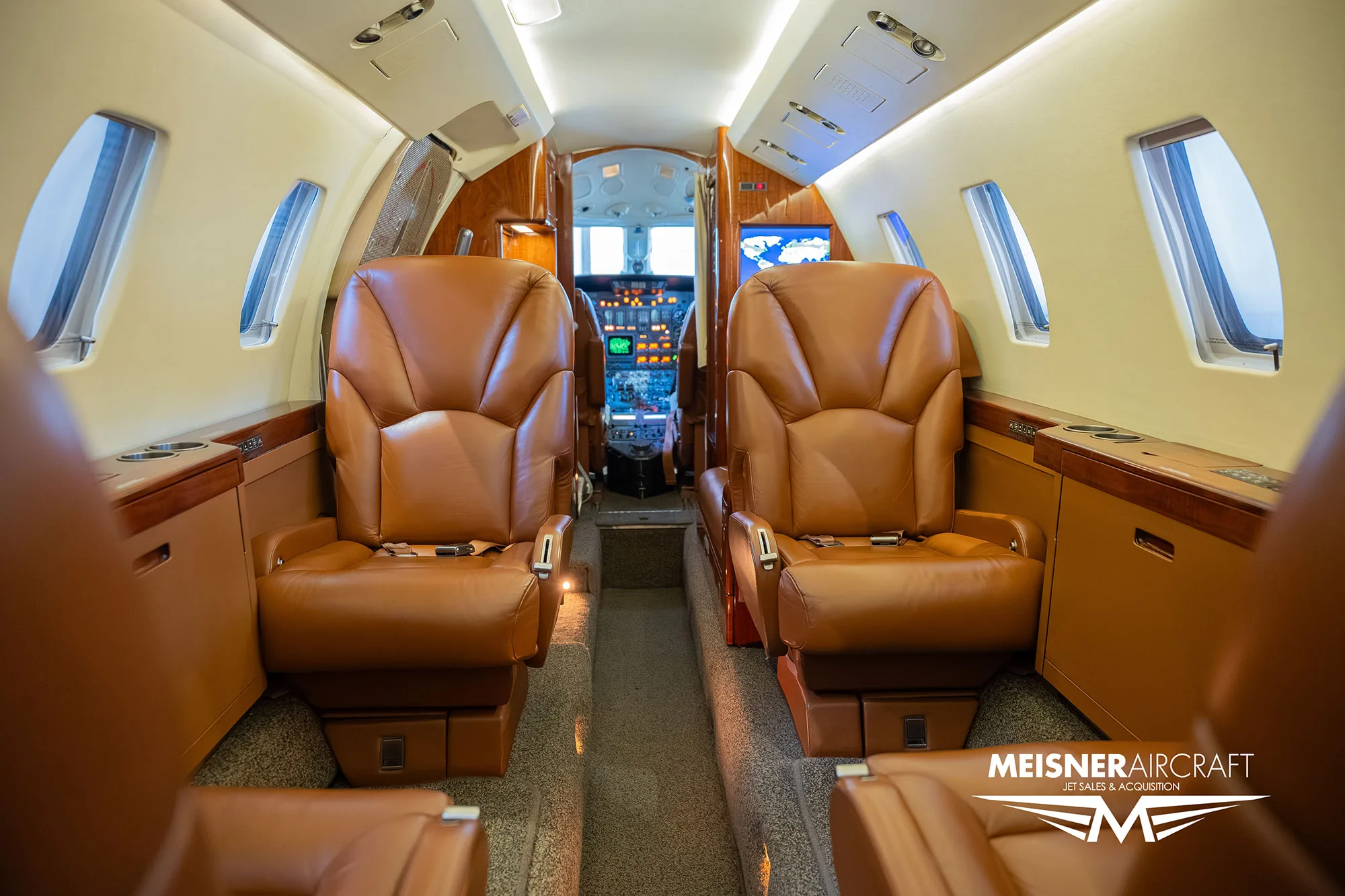 The luxurious interior cabin of a private jet with brown leather seats and a view towards the cockpit.