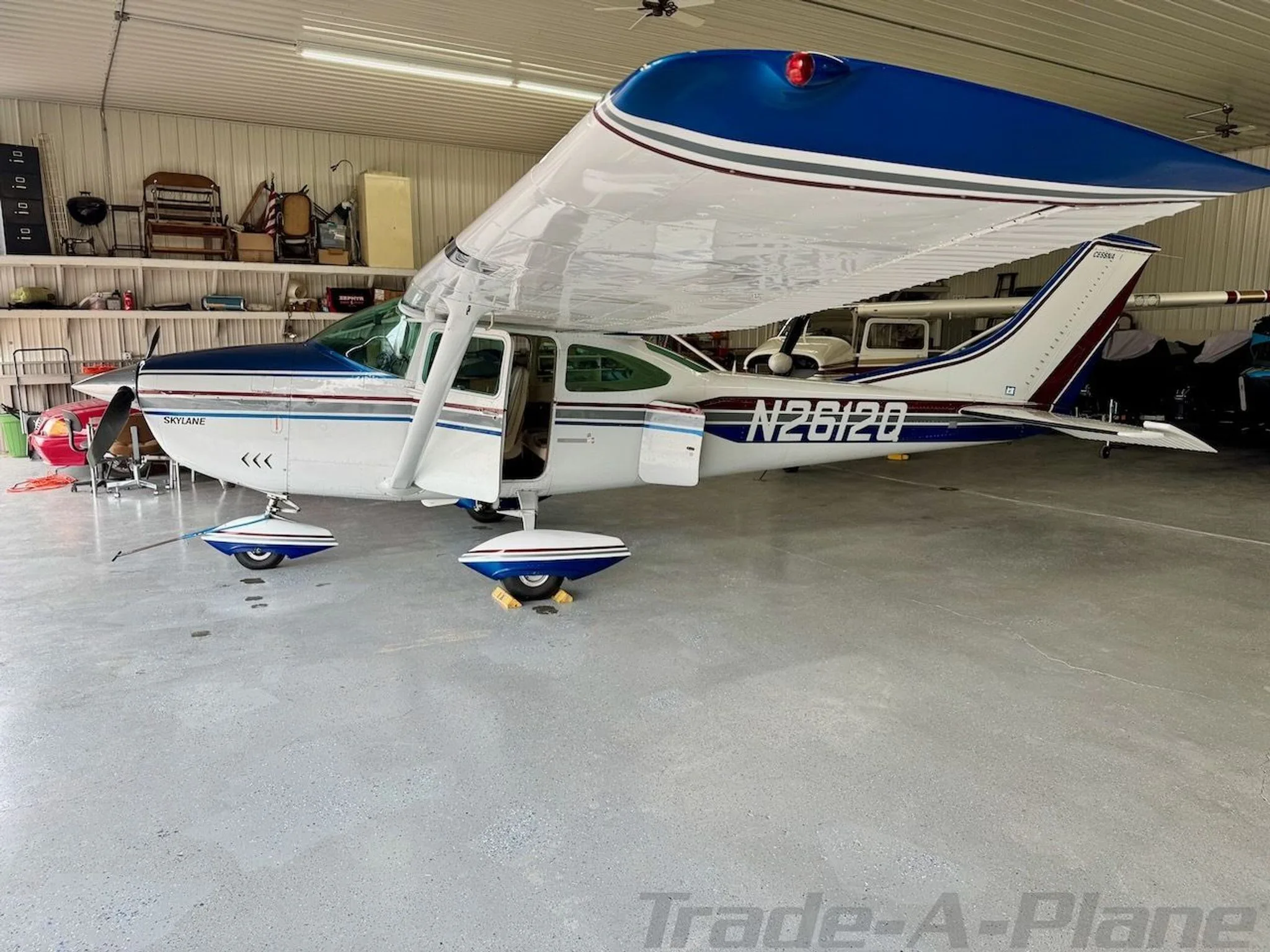 A white and blue Cessna N2612Q Skylane with its door open, parked inside a hangar.