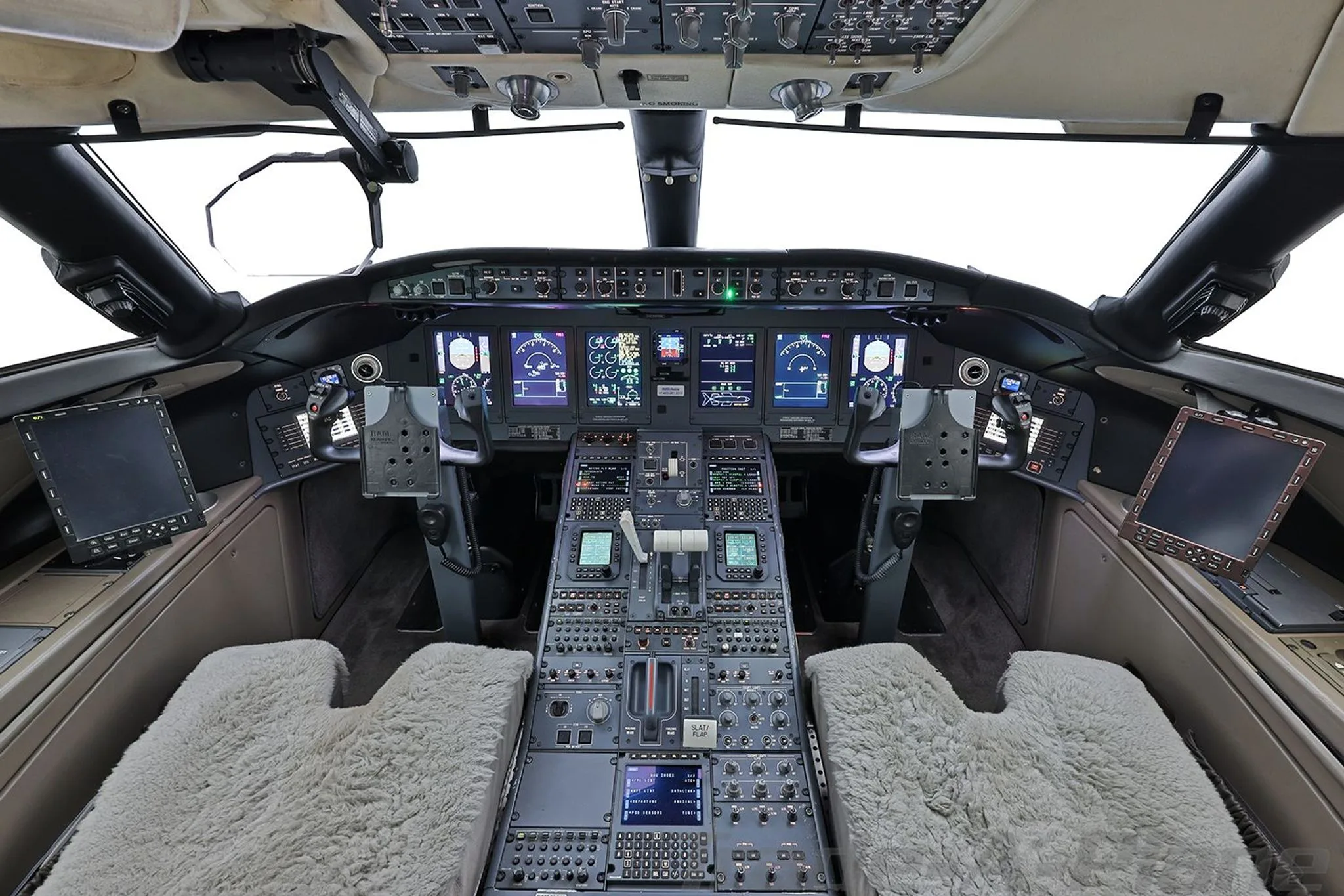The cockpit of a Bombardier Global 6000 business jet, showing the instrument panel and controls with sheepskin seat covers.