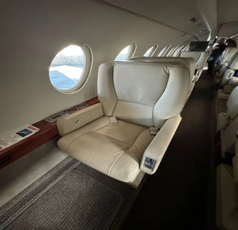 A close-up of a light-colored leather passenger seat in the aircraft cabin next to a window.