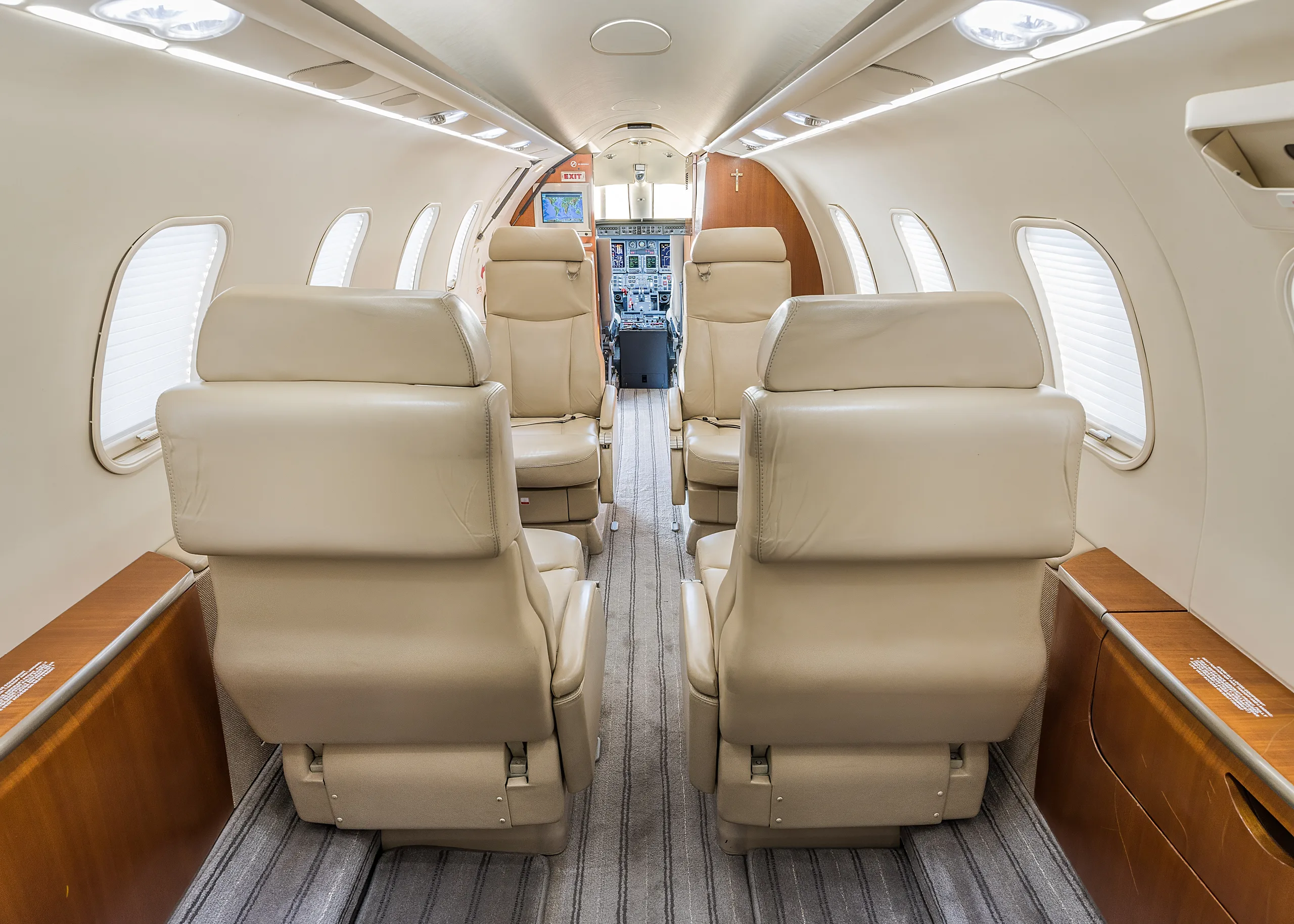 View of the aircraft cabin interior with beige leather seats and a glimpse of the cockpit.