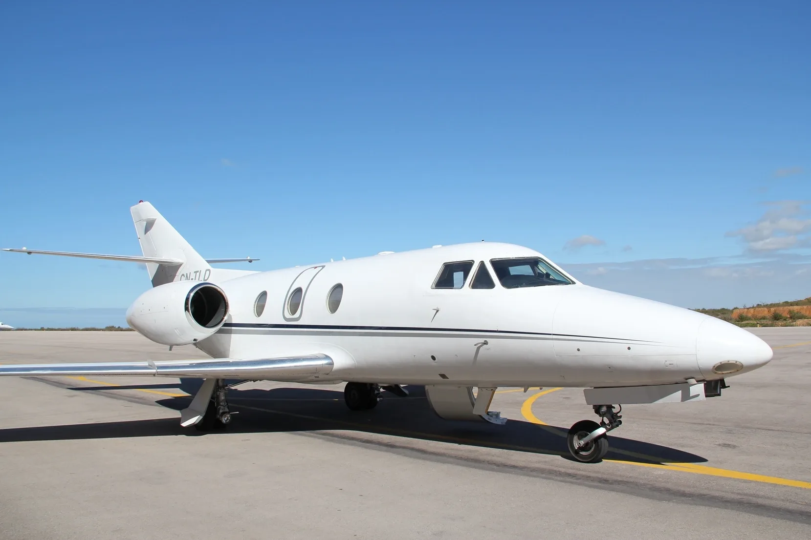 A white business jet, likely a Hawker 800 series with registration CN-TJLD, parked on an airport tarmac under a clear blue sky.