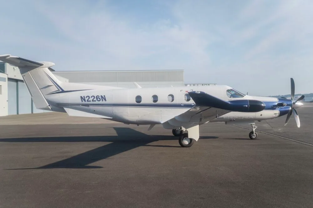 A white and blue Pilatus PC-12 aircraft with registration N226N seen from the right side, parked on an tarmac.