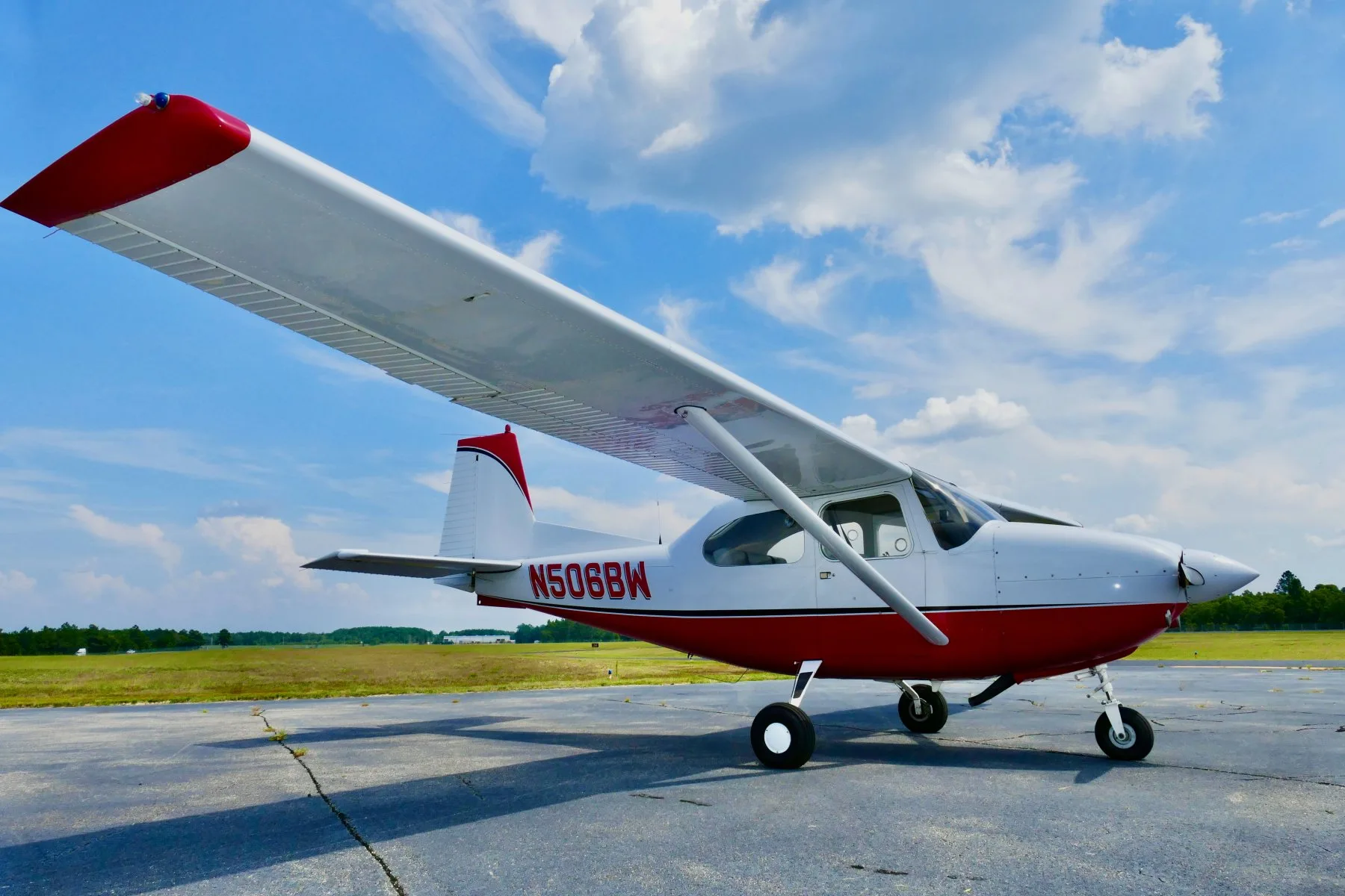 A side-right view of a white and red Cessna 172 aircraft, N506BW, parked on an airfield under a blue sky.