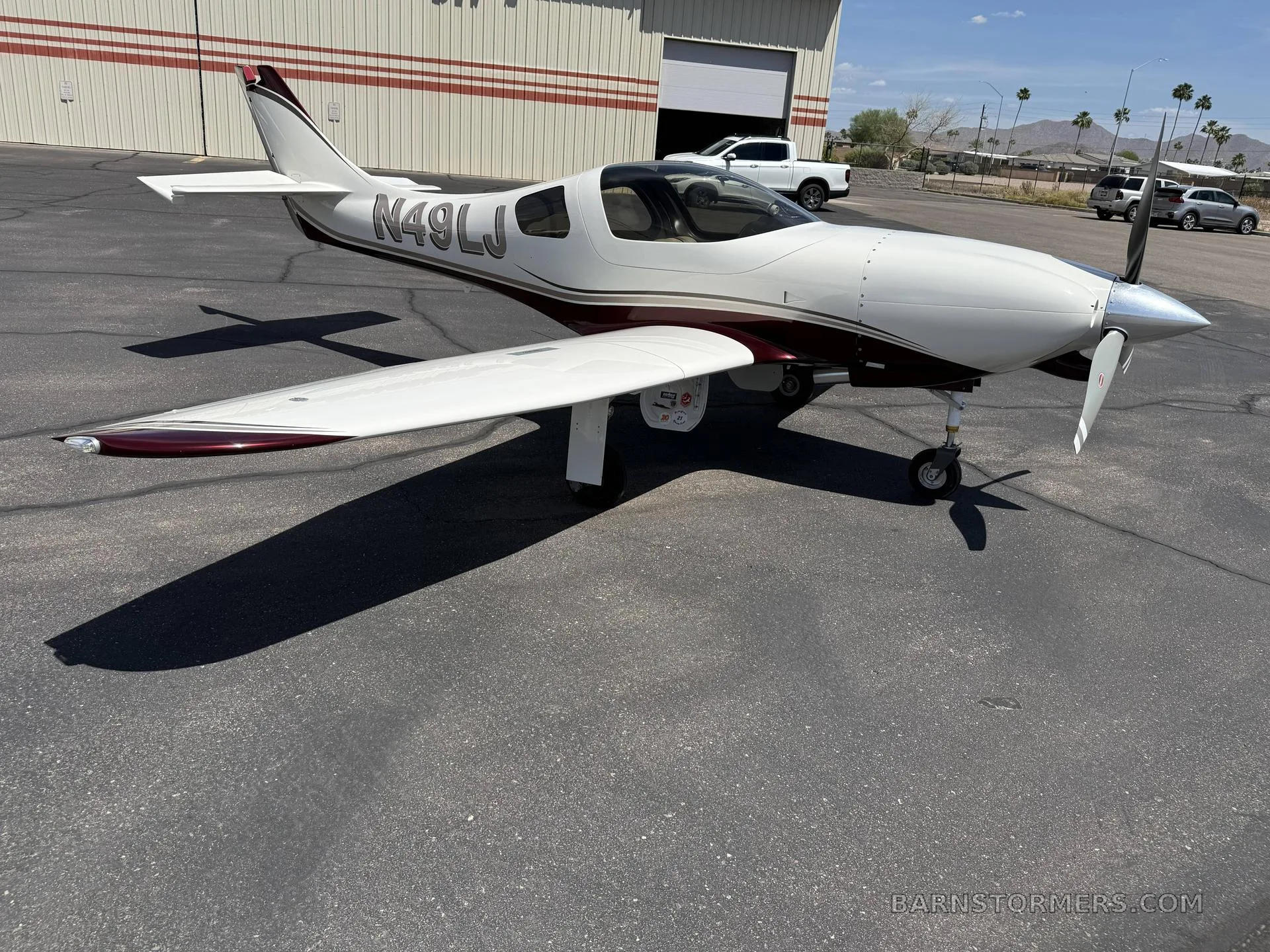A white and maroon single-engine aircraft (N49LJ) with a propeller, parked on an asphalt apron next to a hangar under a clear sky.