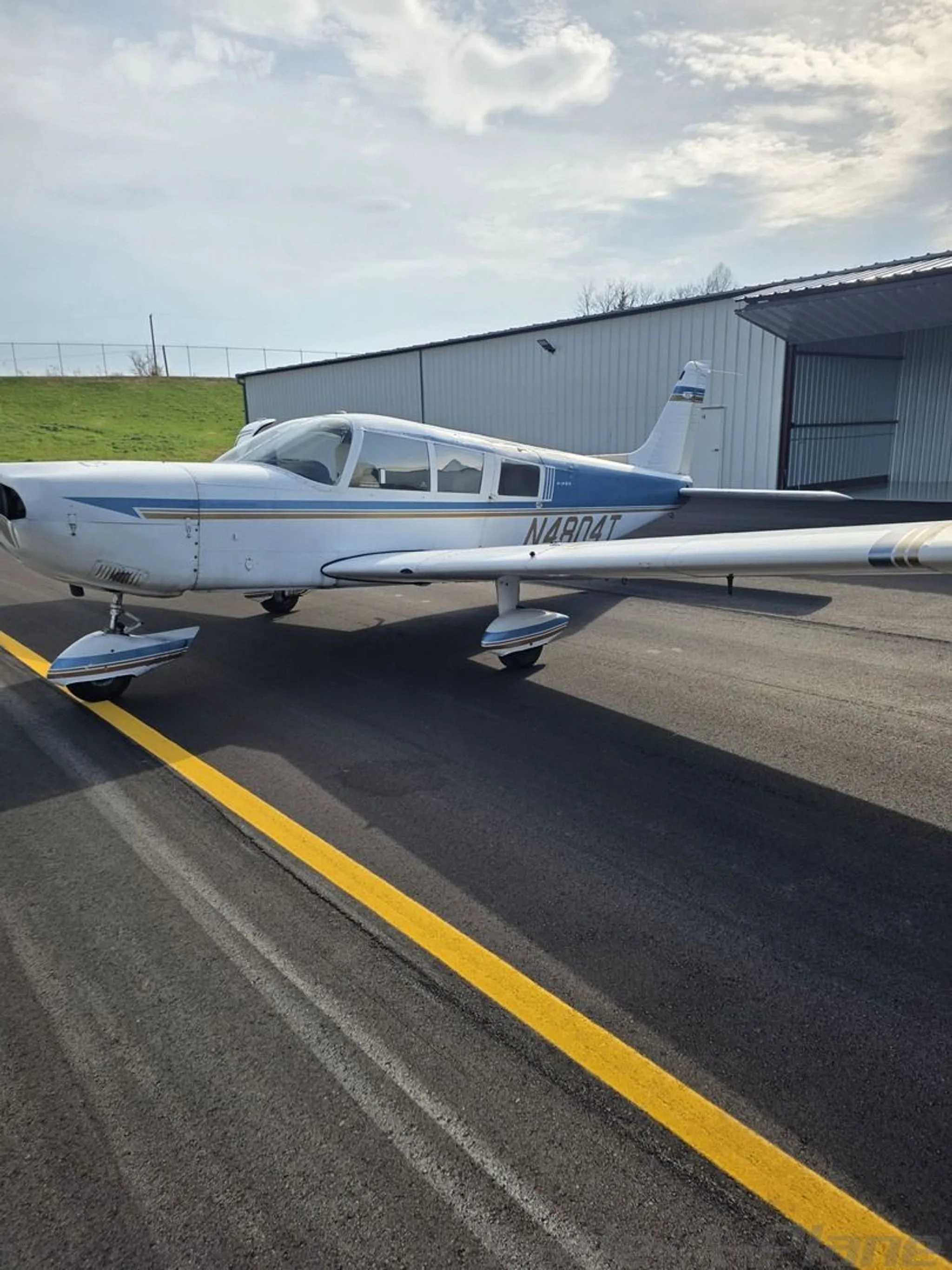 Side view of a white and blue aircraft with registration N4804T parked on a tarmac next to a hangar.