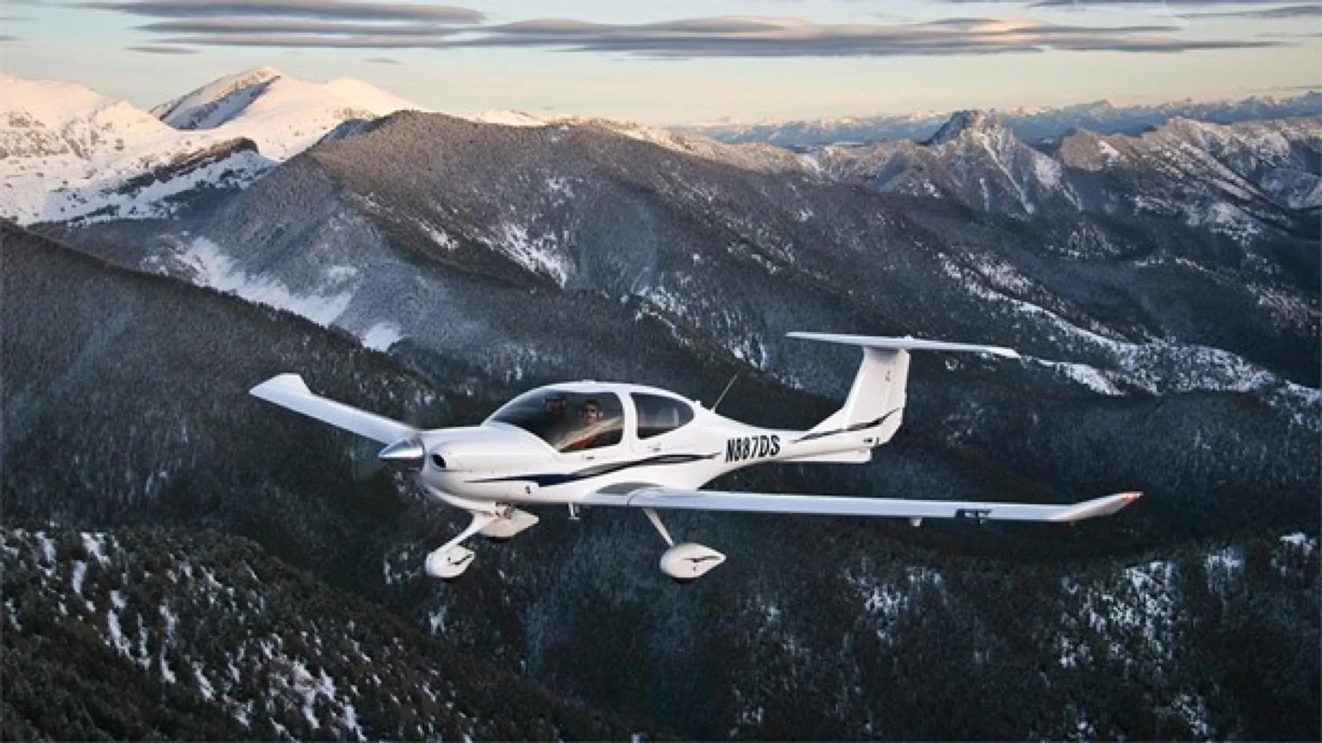 An aerial view of a white Diamond DA40 aircraft, N887DS, flying above snow-covered mountains.