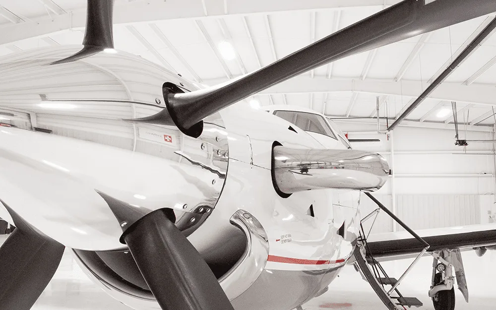 A close-up view of the propeller and nose of a white Pilatus PC-12 aircraft in a hangar.