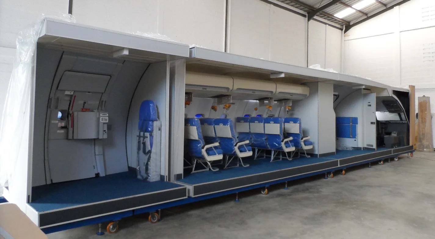 A long training mock-up of an aircraft cabin and cockpit section with blue seats.
