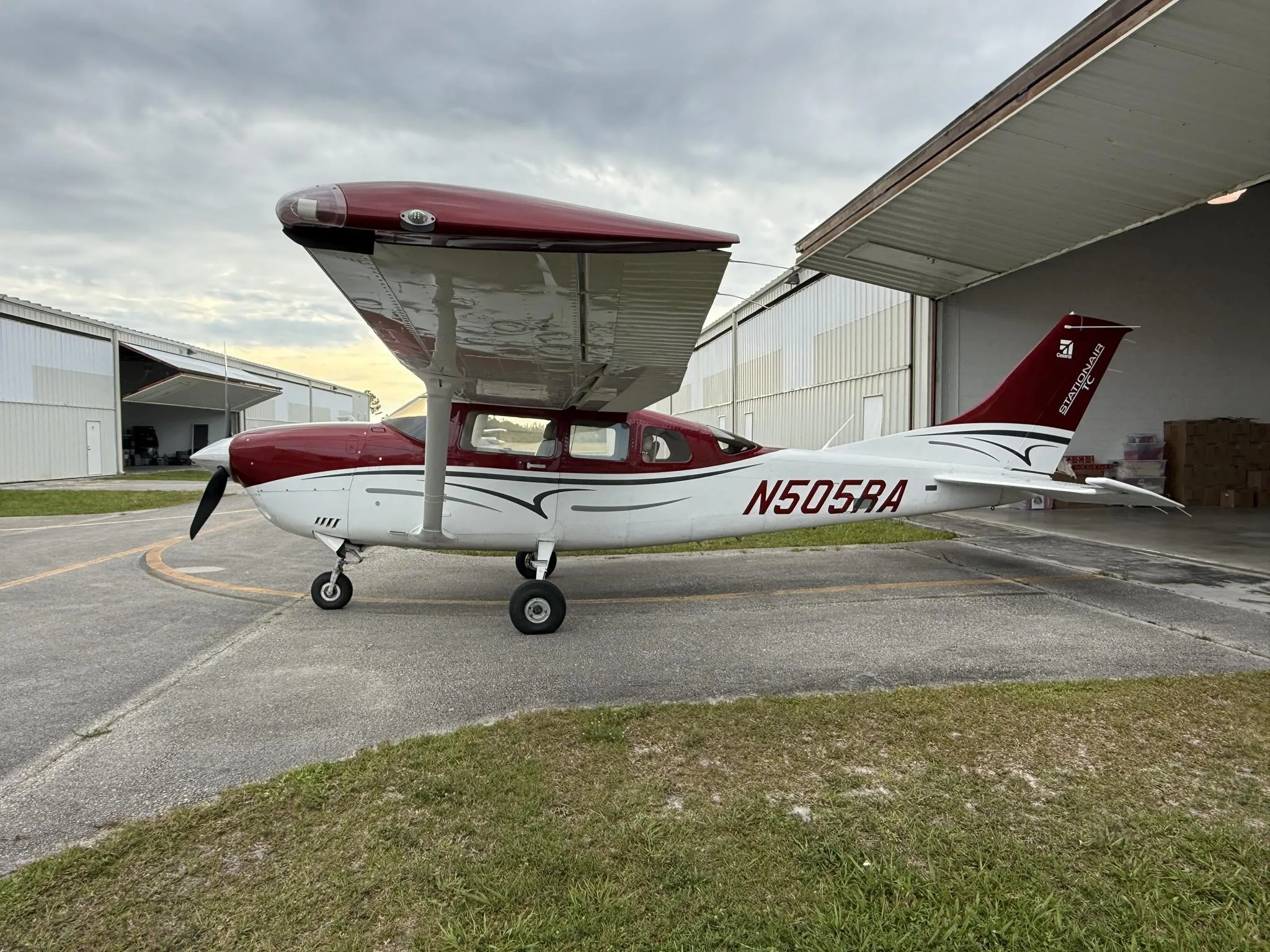 A red and white Cessna Stationair TC aircraft (N505RA) parked outside a hangar, viewed from the left side.