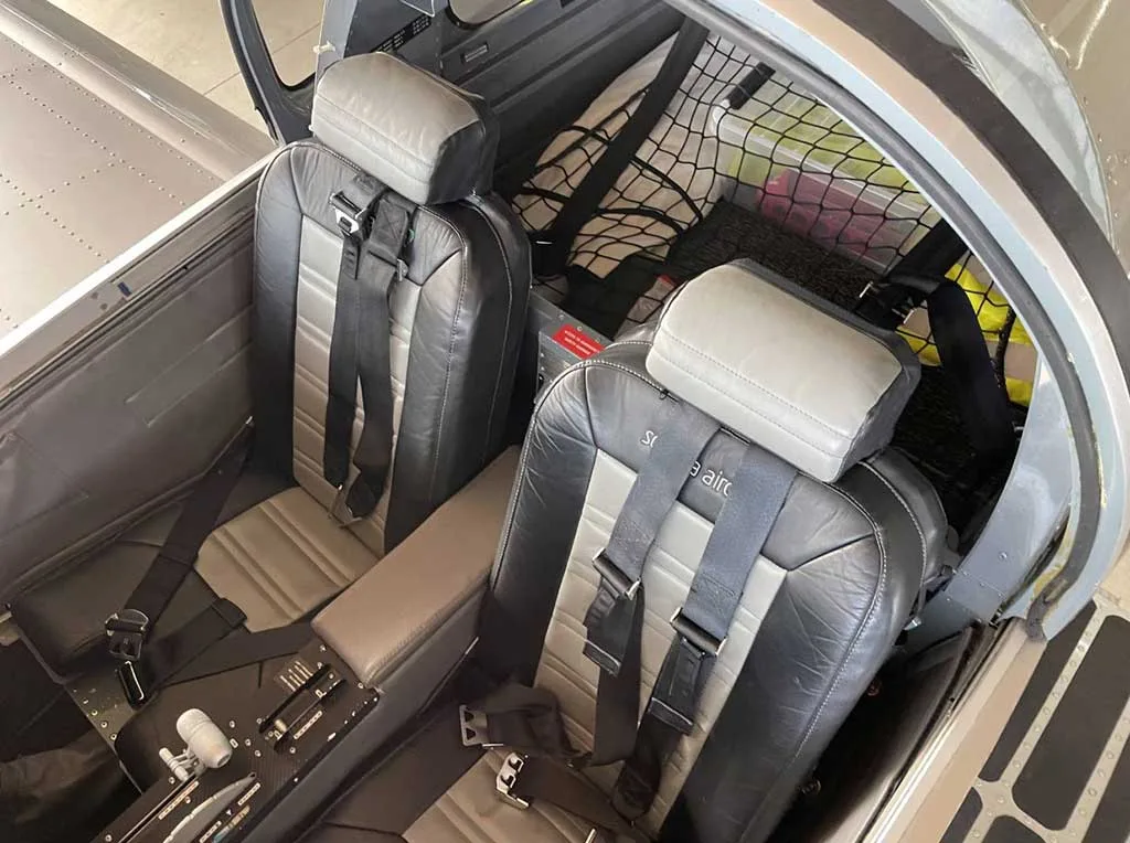 Two grey and black leather seats with harnesses in the aircraft cabin.