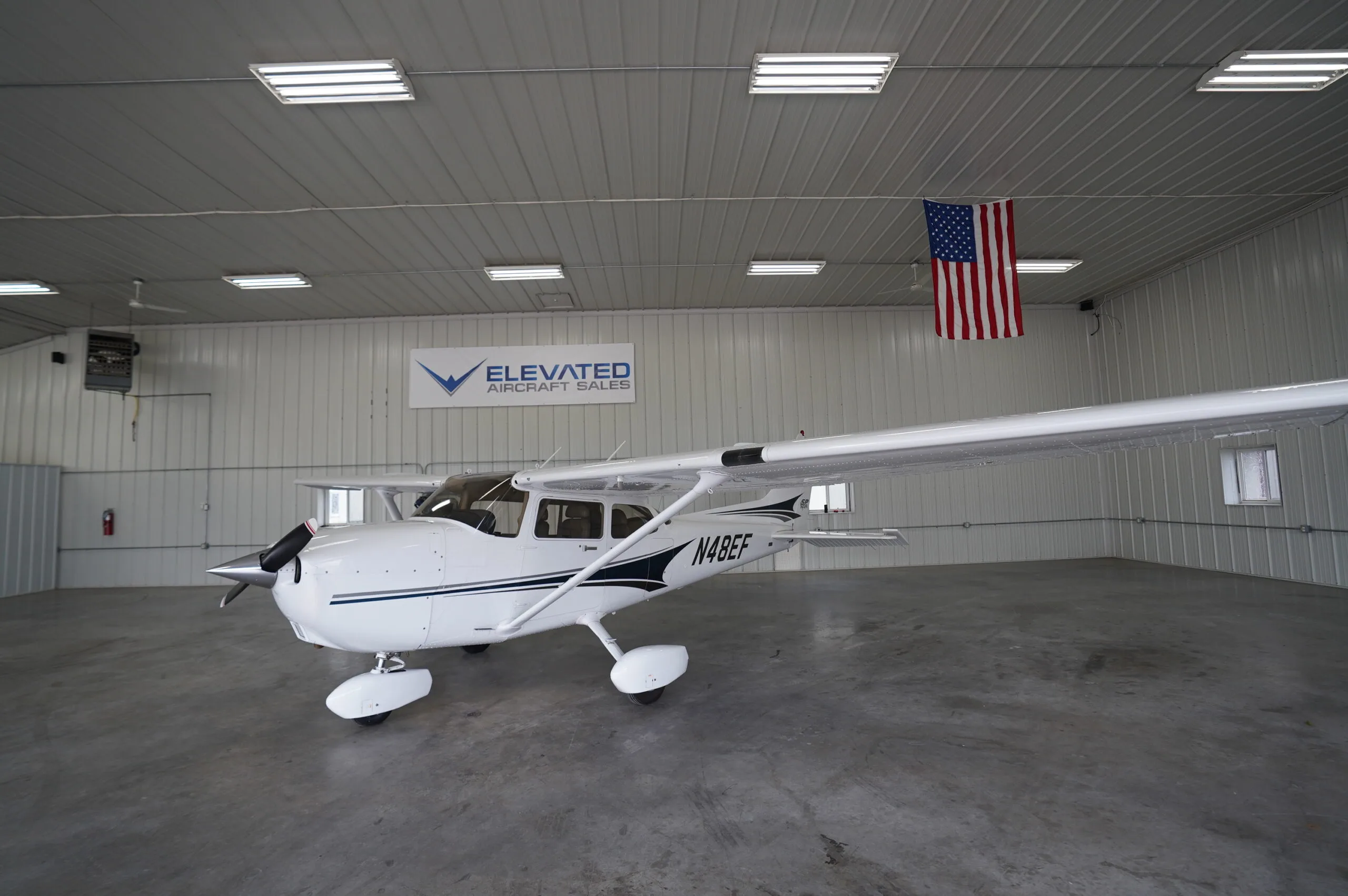 A white Cessna 172 (N48EF) with blue and black stripes parked in a hangar.