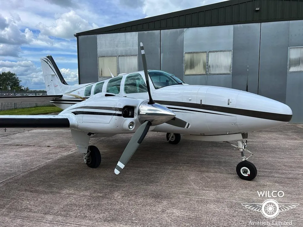 A close-up view of the front right side of a white Beechcraft Baron N142TW with black and gold stripes.