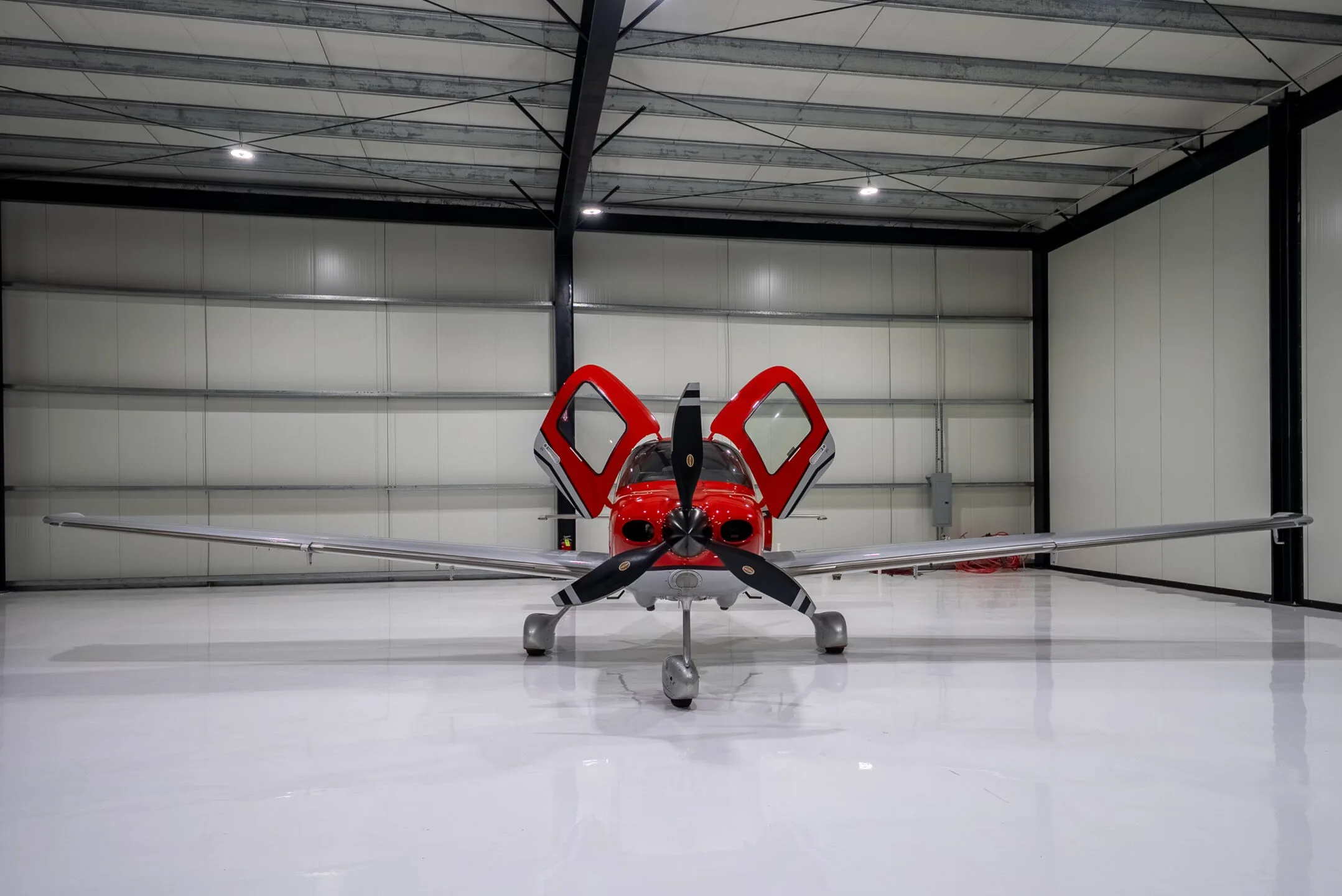 Front view of a red and silver Cirrus SR22T Carbon aircraft with registration N48JN and open doors, in a hangar.