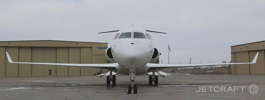 A white Bombardier Global 7500 business jet is seen from the front, parked on an airfield with hangars in the background.