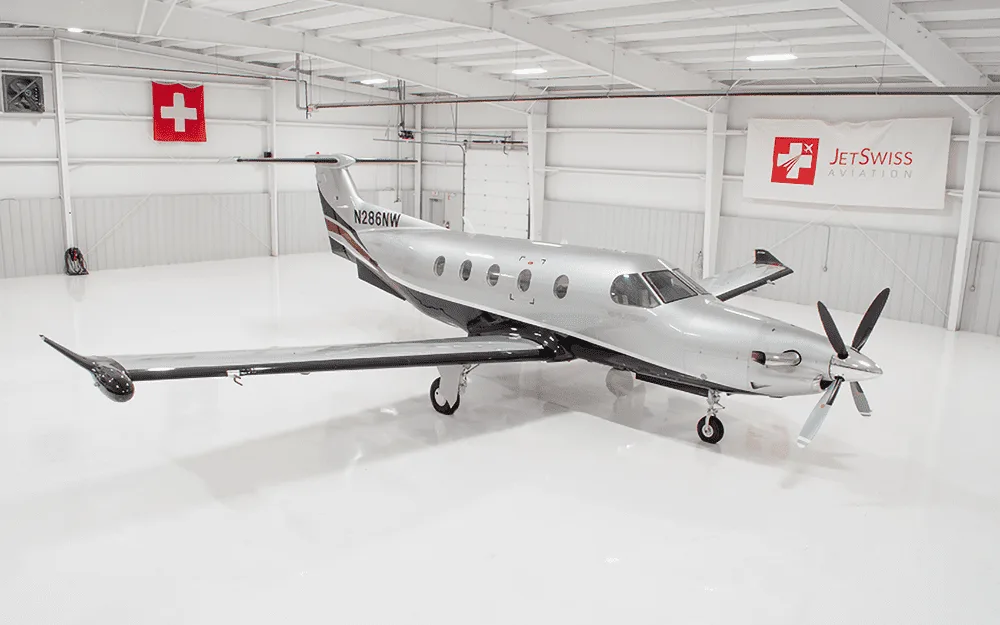 A silver and black Pilatus PC-12 NG aircraft with registration N286NW parked in a brightly lit hangar.