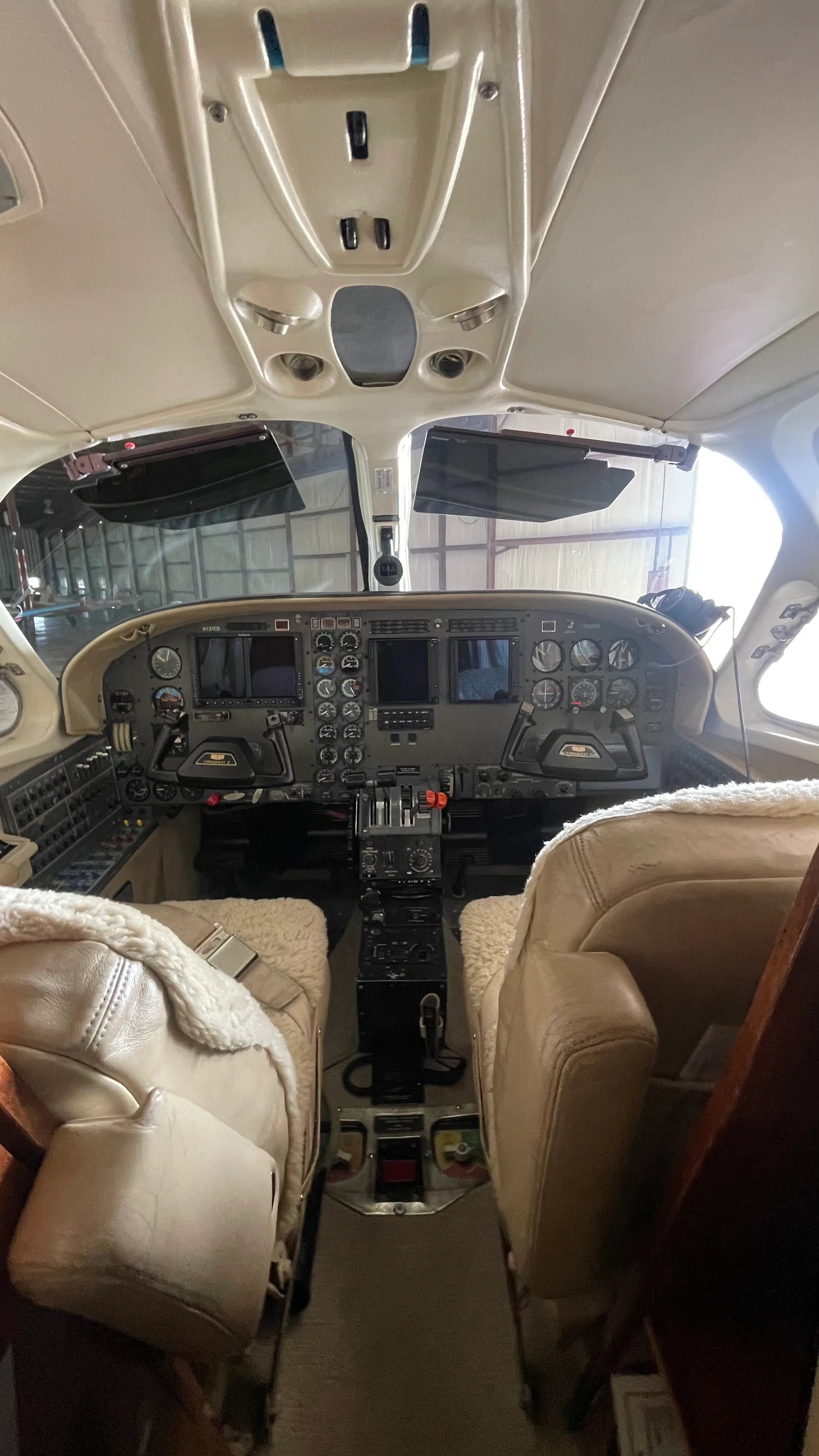A view of the aircraft's cockpit with instrument panel, yokes, and tan sheepskin-covered pilot seats.