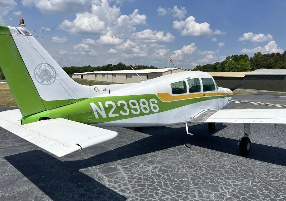 Rear-side view of a white and green Beechcraft Sundowner 180 (N23986) showing the tail and registration.
