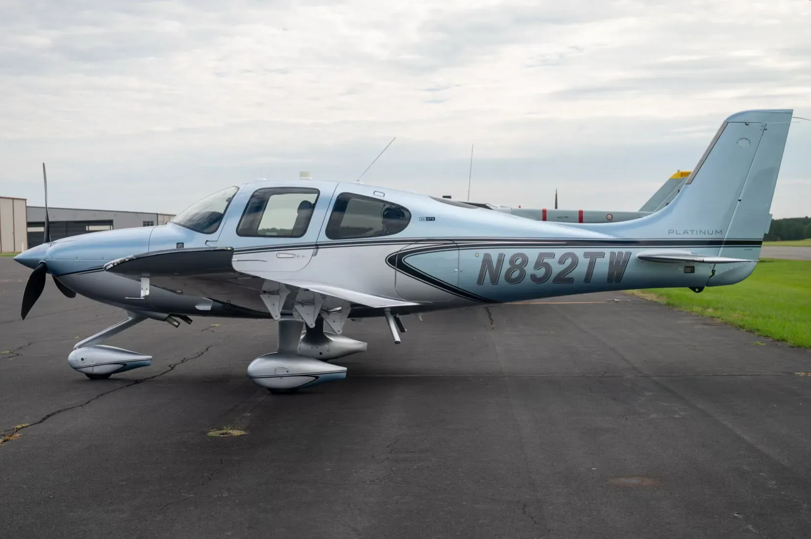 A three-quarter side view of a blue and silver Cirrus SR22 aircraft, N852TW, parked on an asphalt tarmac.