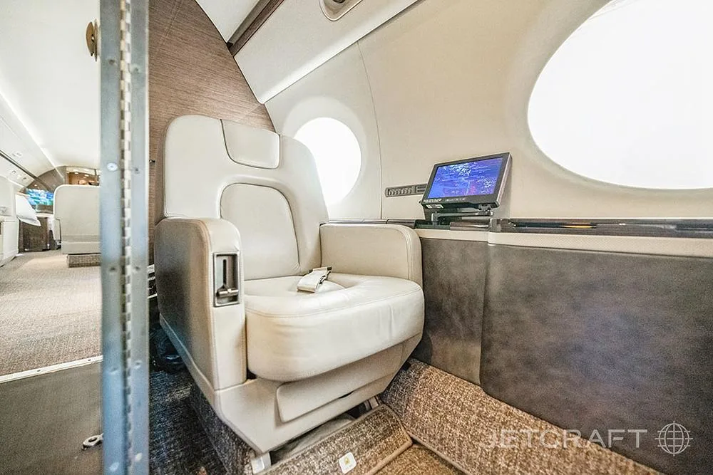 A close-up of a cream leather seat in the Gulfstream G650 cabin with a personal entertainment screen.