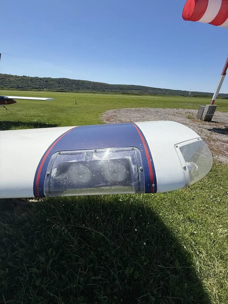 A close-up view of the wingtip and landing lights of the blue and white Socata Trinidad aircraft.