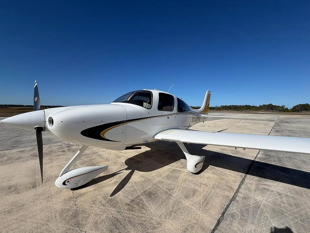 A front-left view of a white Cirrus SR22 aircraft with black and gold stripes, registration N583PU, parked on an airfield.