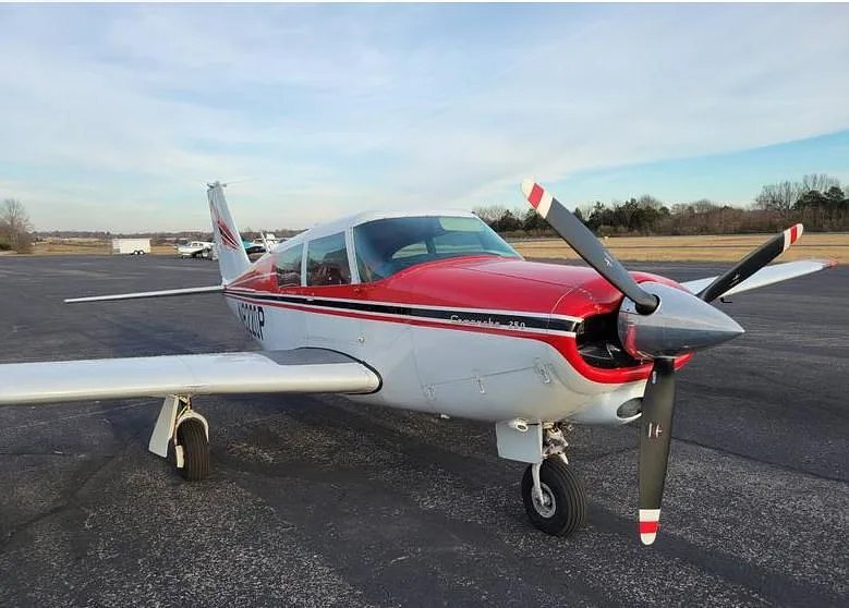 A front-right view of a red and white Piper Comanche 250 aircraft, tail number N8220P, parked on an airfield.