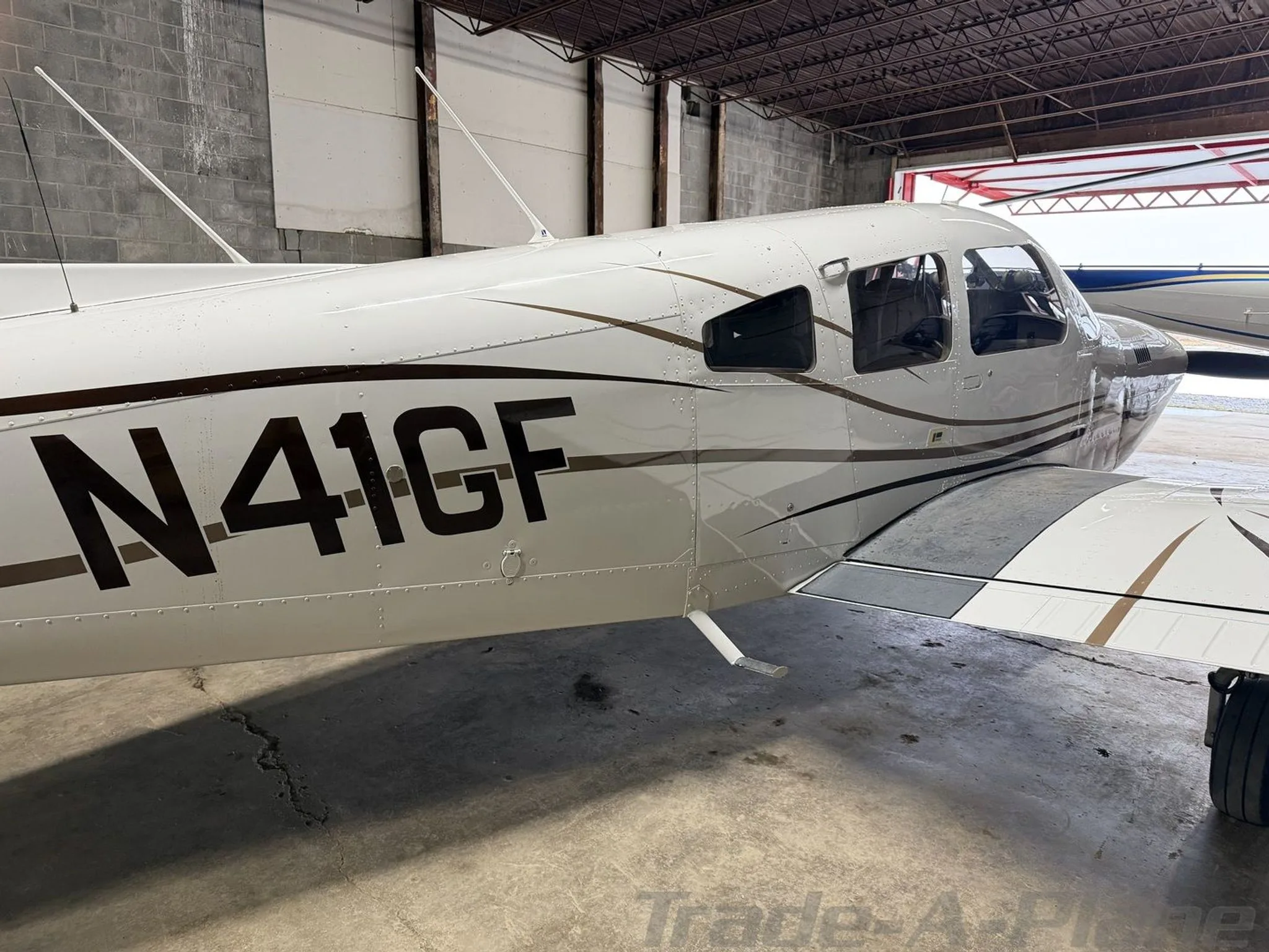 A close-up side view of the white Piper aircraft N41GF with brown stripes, parked in a hangar.