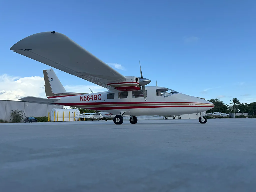 A white and red twin-engine aircraft, N564BC, is parked on an airport tarmac under a blue sky.