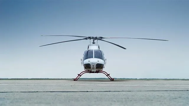 A white and red helicopter with skids on a tarmac under a clear blue sky, viewed from the front.