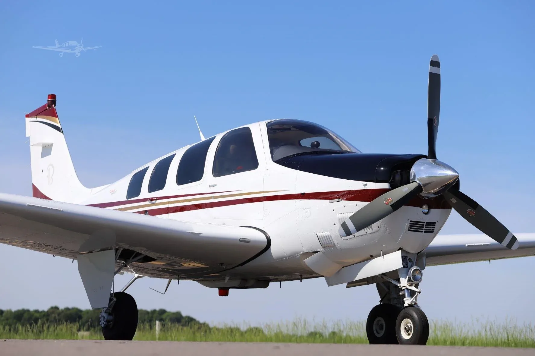A white and black single-engine propeller aircraft with red and gold stripes, viewed from the front-right on a tarmac.