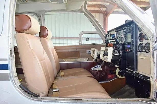 The tan leather front seats and side panel of a general aviation aircraft cabin, with a partial view of the cockpit.
