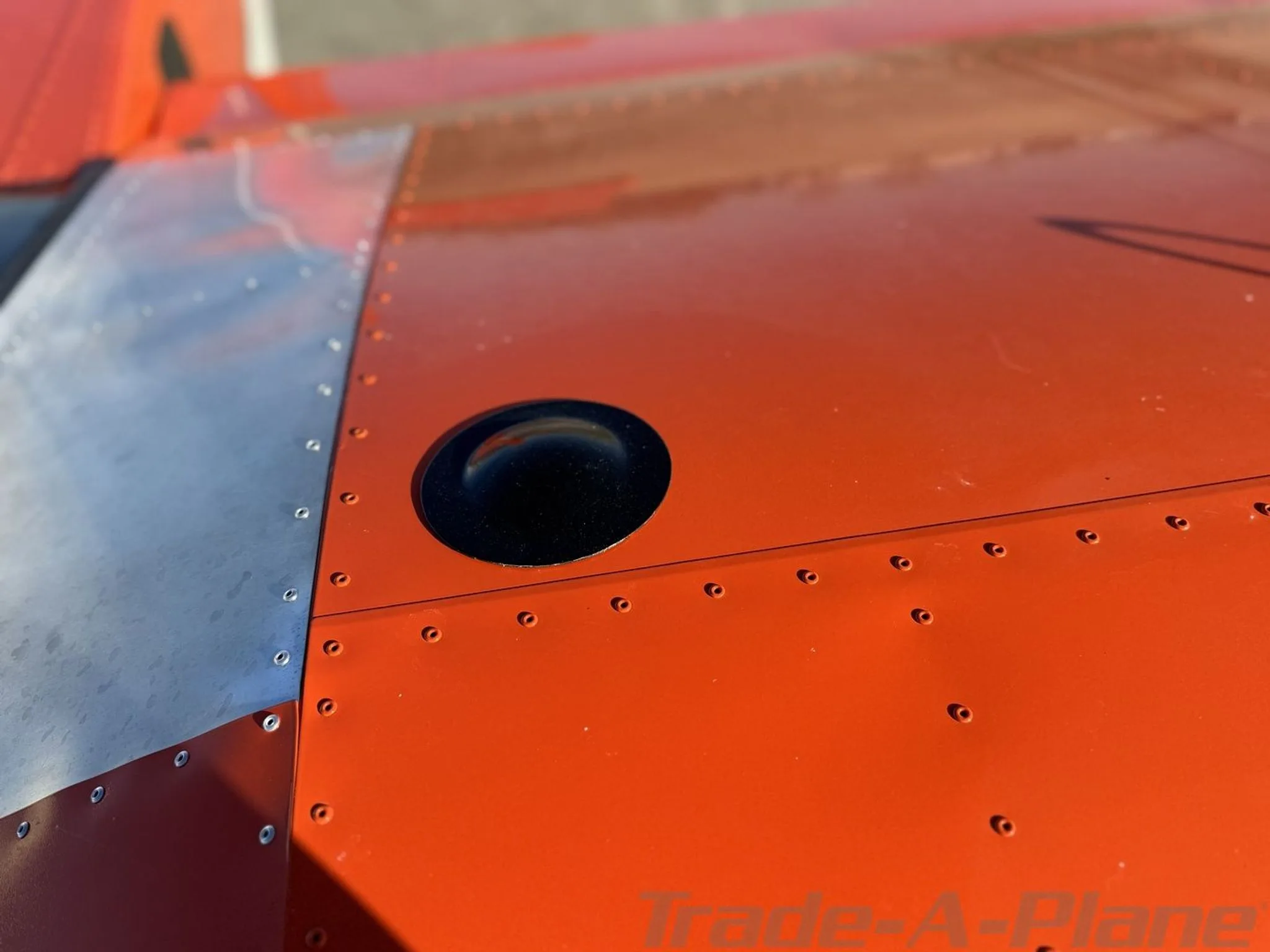 Close-up view of a fuel cap or inspection port on the orange and silver wing of an aircraft.