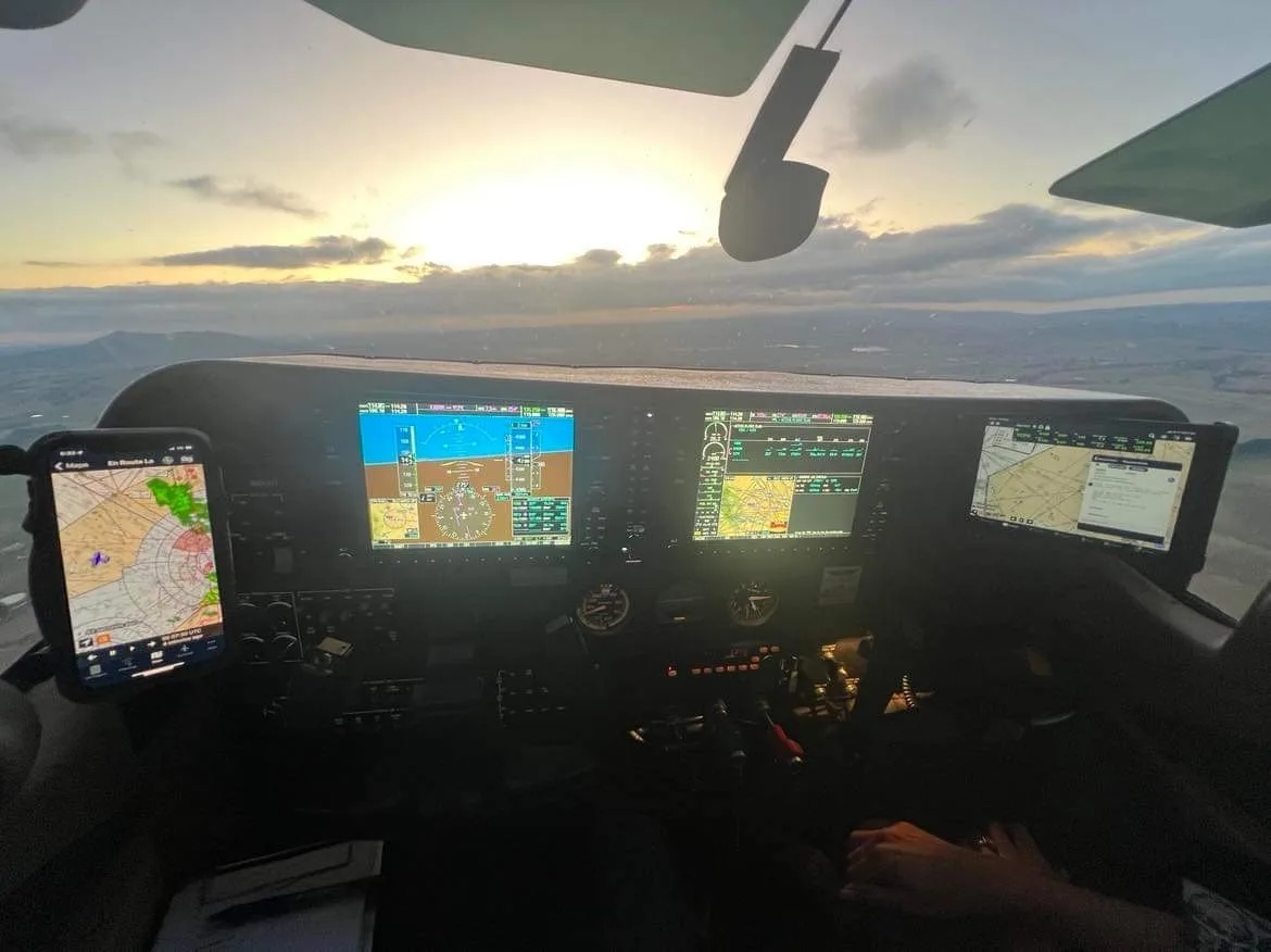 A modern glass cockpit with multiple screens and a phone mount, showing a sunset view from the aircraft.