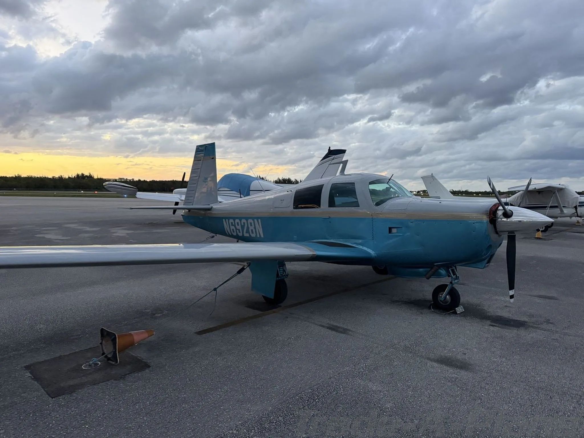 A light blue and white single-engine aircraft, N6928N, parked on an airport tarmac at dusk under an overcast sky.