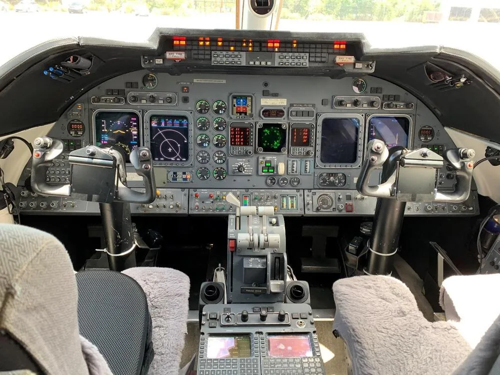 The cockpit of a private jet, featuring a complex instrument panel with multiple displays, yokes, and controls.