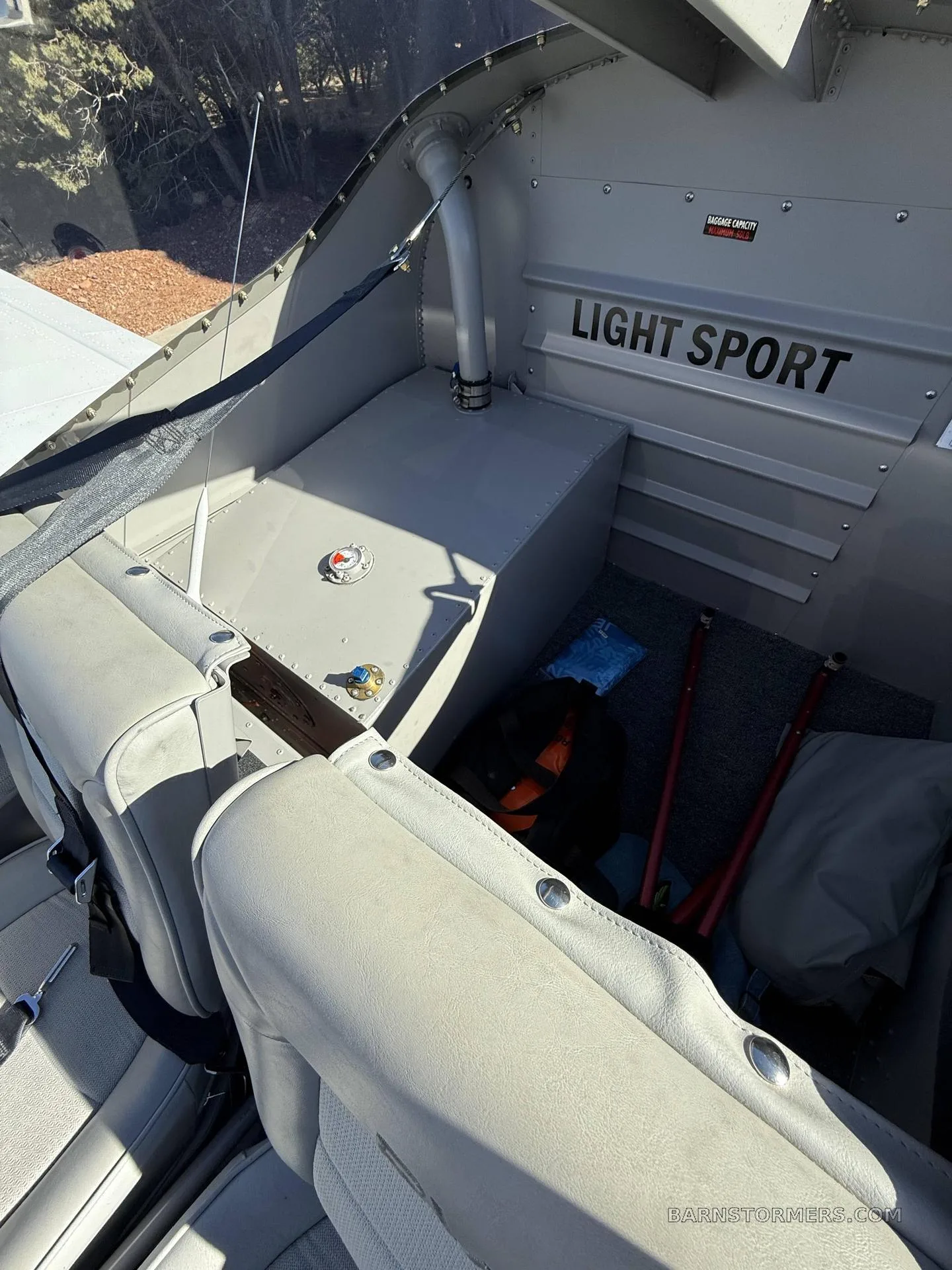 The rear interior of an RV-12 aircraft shows a storage area behind the light gray seats with "LIGHT SPORT" text on the wall.
