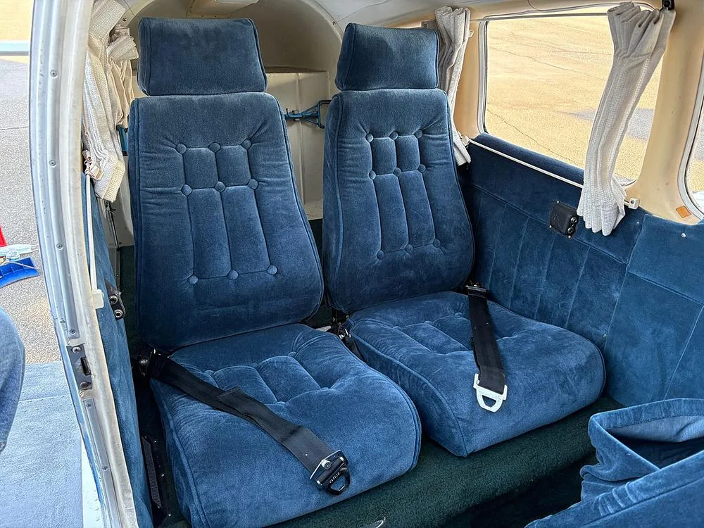 Two rows of plush blue velour passenger seats with seatbelts in the aircraft cabin.