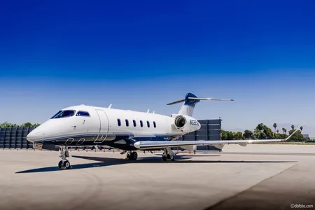 A white and blue Bombardier Challenger business jet parked on an airport tarmac under a clear blue sky.