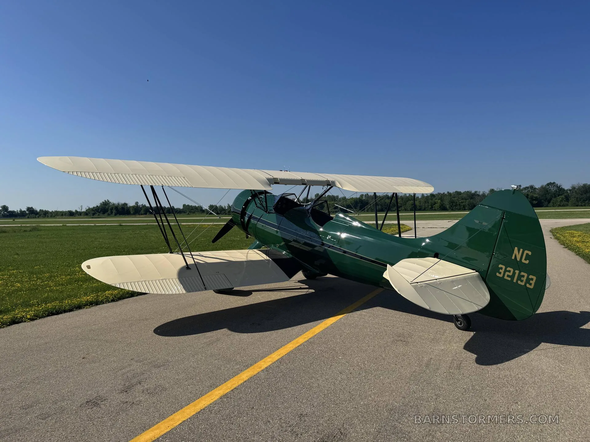 The rear view of a green and cream biplane with registration NC 32133 on its tail, parked on an asphalt runway.