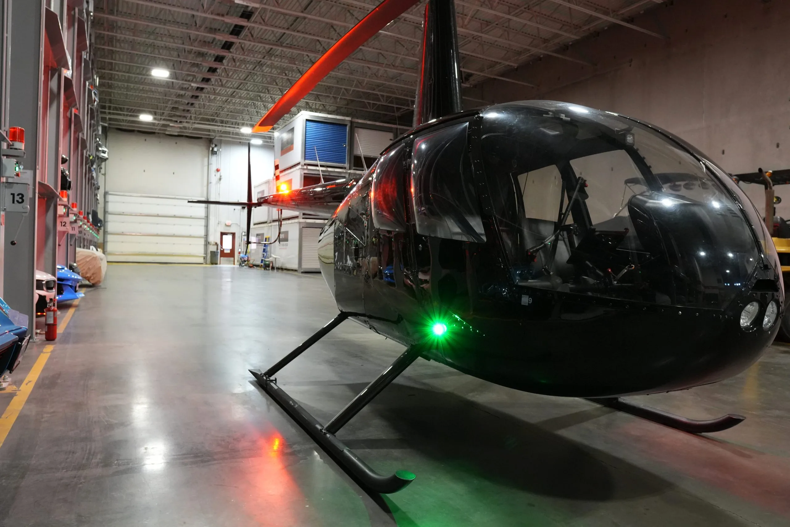 A black Robinson R44 helicopter with green and red lights on, parked in a hangar.