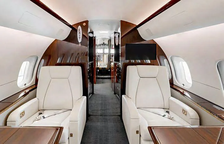 The luxurious interior cabin of a business jet with cream leather seats and dark wood accents.
