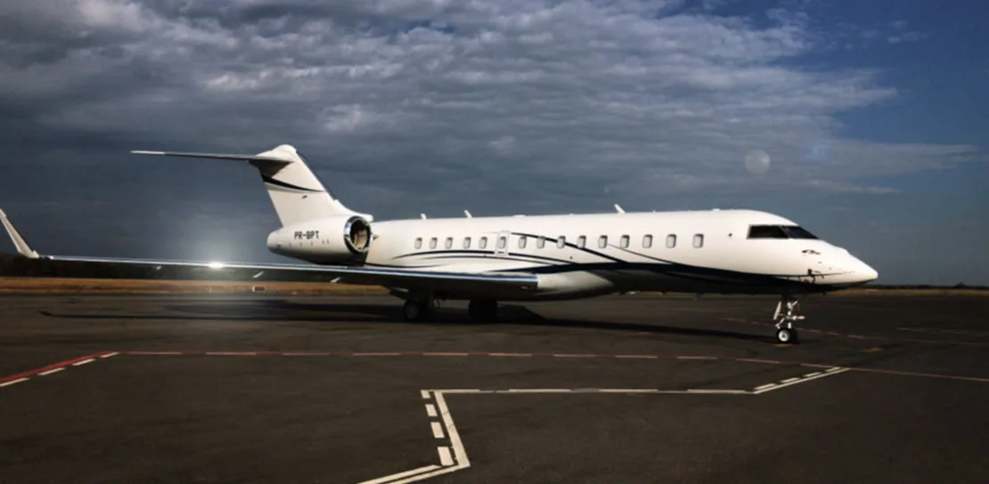A white private jet with a dark blue stripe and registration PR-BPT is parked on an asphalt tarmac under a cloudy sky.