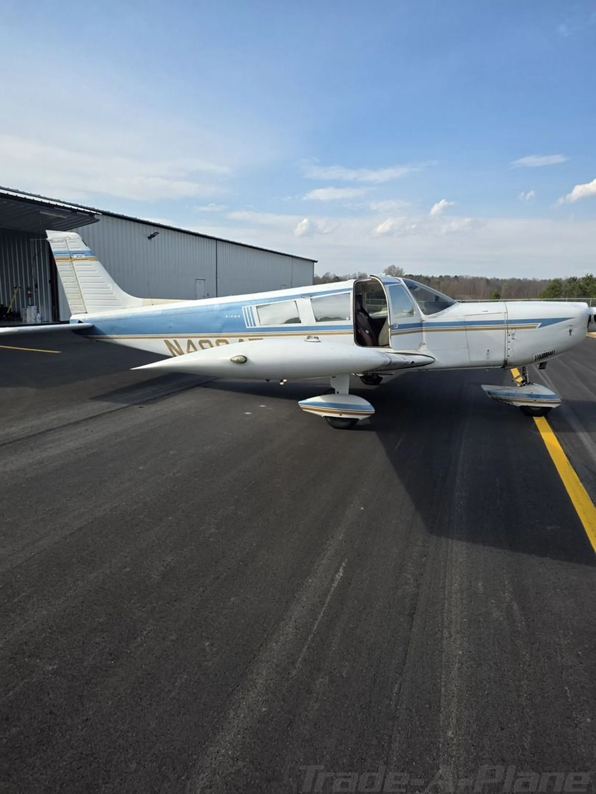 Side view of a white and blue aircraft with an open door parked on a tarmac next to a hangar.